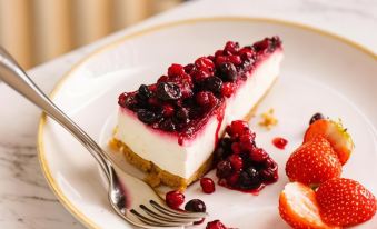 a white plate with a slice of cheesecake on it , accompanied by a fork and a spoon at Leonardo Hotel Middlesbrough - Formerly Jurys Inn