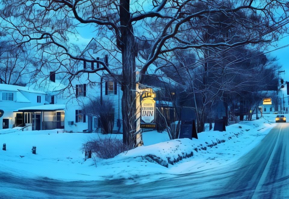 a snow - covered street with a large tree and a building , creating a picturesque winter scene at Dowds Country Inn
