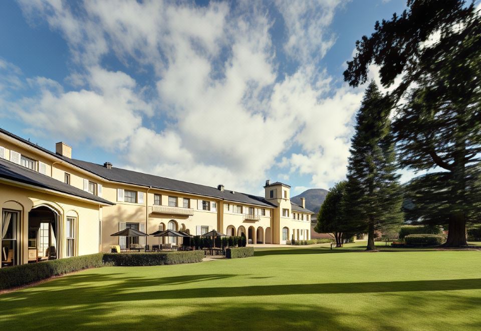 a large building with a green lawn and trees in front of it , under a blue sky with clouds at Hanmer Springs Hotel