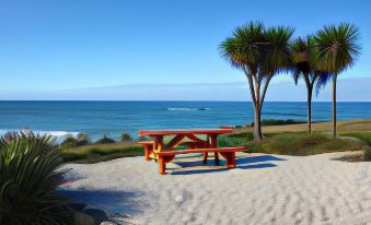 a wooden picnic table is set up on a sandy beach near the ocean , with palm trees in the background at Saltwater - Absolute Oceanfront, Hot Tubs, Sauna, Fire Pits