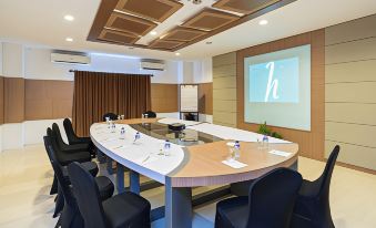 a conference room with a round table , chairs , and a projector screen displaying a letter at Horison Tirta Sanita Kuningan