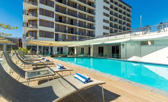 an outdoor swimming pool surrounded by a hotel building , with lounge chairs and umbrellas placed around the pool area at Pacific Hotel Cairns