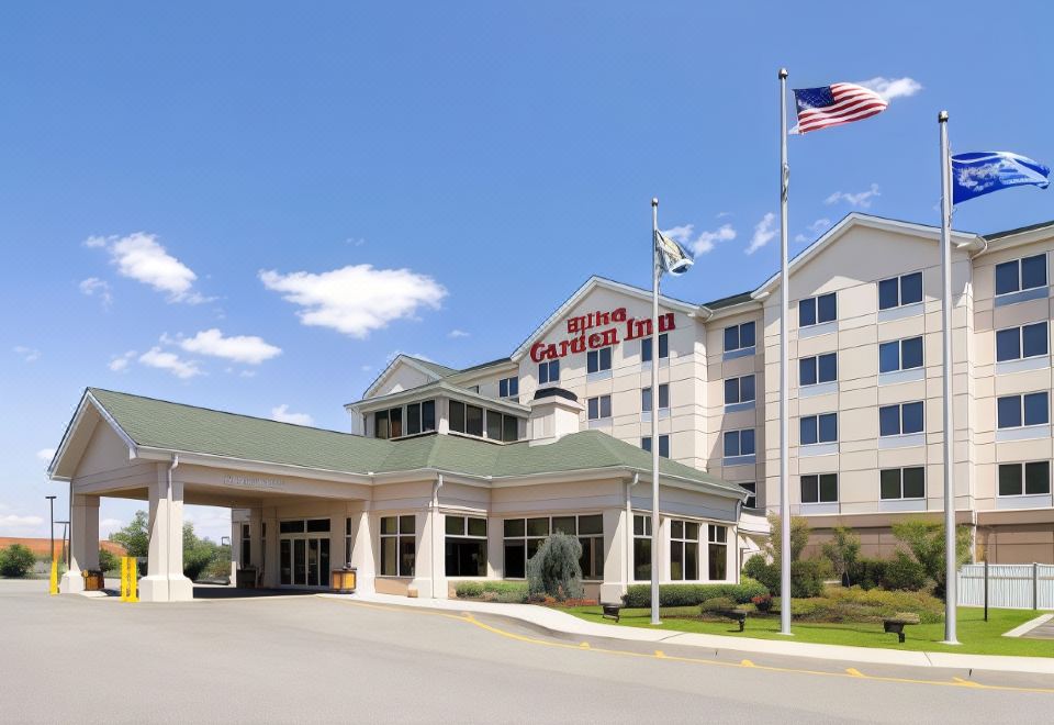 a large hotel with a green roof and american flag on top , under a clear blue sky at Hilton Garden Inn Nanuet