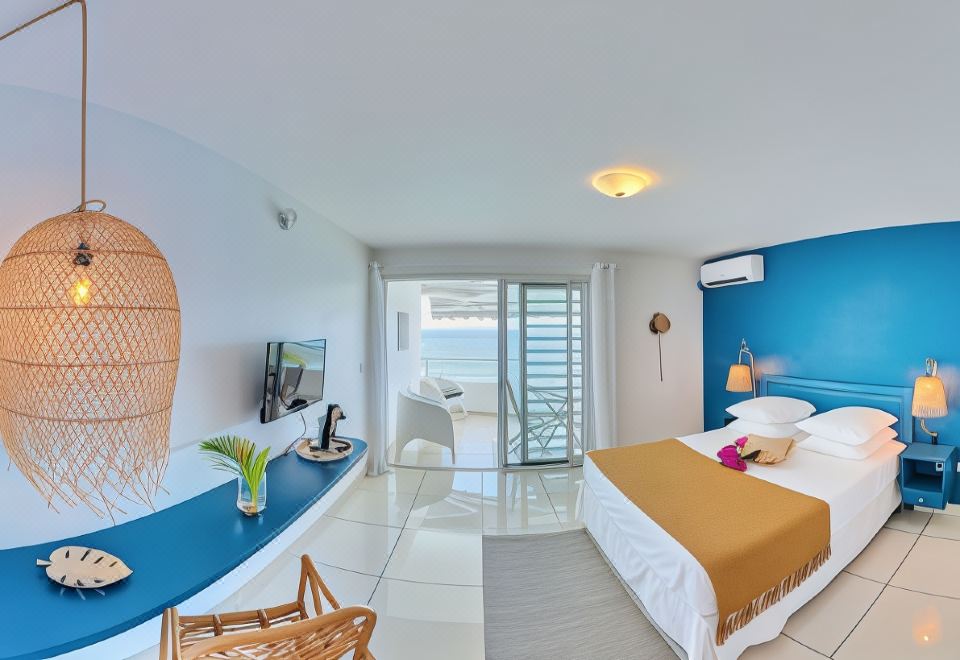 a bedroom with a blue wall and a balcony overlooking the ocean , featuring a bed , desk , and tv at Hotel Pelican