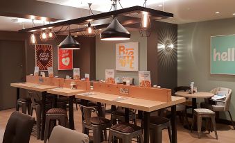 a restaurant with wooden tables and chairs , a large central feature , and black pendant lights at Premier Inn Caerphilly (Corbetts Lane)