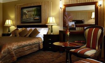 a hotel room with a king - sized bed , two chairs , and a table , along with various decorative items at Riverside Inn