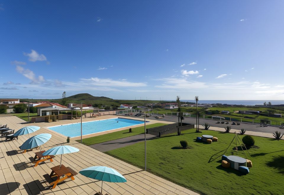 a large outdoor pool area with umbrellas , chairs , and lounge chairs , surrounded by a grassy field at Hotel Colombo