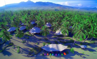 an aerial view of a campsite with multiple tents and palm trees , surrounded by mountains at Coconut Garden Beach Resort