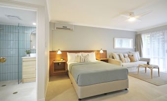 a well - lit bedroom with a bed , nightstands , and lamps , as well as a couch in the background at Bay of Palms