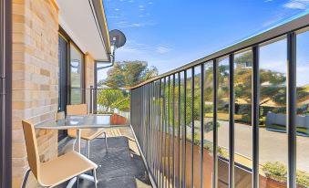 a balcony with a dining table , chairs , and a fence , overlooking a green landscape under a clear blue sky at Lemon Tree Passage Motel