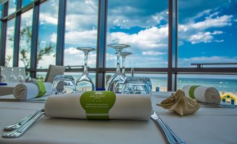 a table is set with wine glasses , napkins , and a bottle of water in front of a window at San Marco