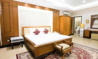 a large bed with a wooden headboard and white linens is in a room with a red rug , wooden furniture , and a chair at Hotel Cianjur Cipanas