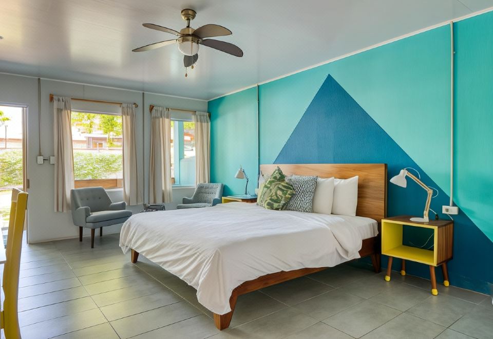 a cozy bedroom with a large bed , a fan , and various decorative items such as pillows and a painting at Selina Jaco