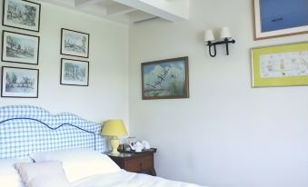 a cozy bedroom with a blue and white checkered headboard , framed paintings on the wall , and a bedside table at Stone House