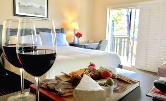 a glass of wine and a plate of cheese with fruit are placed on a table in front of a bed at The Olympia Lodge