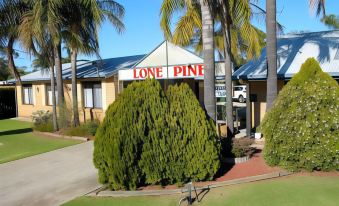 a lone pine motel with a green lawn , palm trees , and a white building in the background at Lone Pine Motel