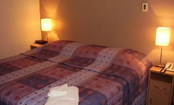 a bed with a colorful patterned blanket and two folded white towels on top of it at Lucas Heights Motel