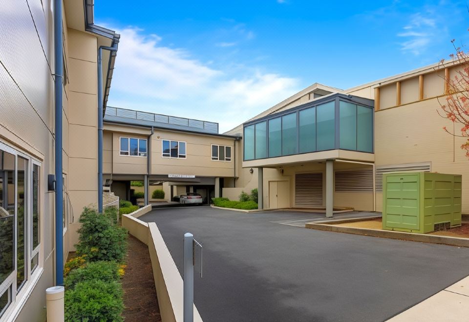 a modern , beige - colored building with large windows and balconies , situated on a street with greenery and a clear blue sky at Lithgow Workies Club Motel