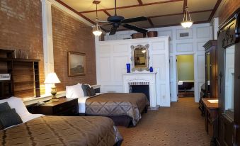a hotel room with two beds , a fireplace , and a brick wall , decorated with curtains and ceiling fans at Iron Horse Hotel