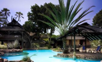 a large outdoor swimming pool surrounded by palm trees , with several people enjoying their time in the pool at Sarova Shaba Game Lodge