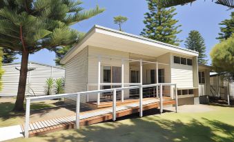 a small house with a wooden deck and a metal railing , surrounded by trees and grass at Nrma Sydney Lakeside Holiday Park