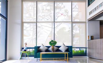 a living room with a blue couch , yellow table , and large windows that offer views of an artistic design at Fortune Hotel Buriram