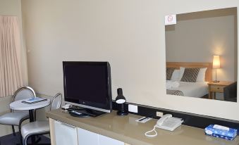 a computer monitor is on a desk next to a phone and a cup , with a window reflecting a bed in the background at Best Western Mahoneys Motor Inn