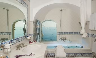 a luxurious bathroom with a bathtub and a view of the ocean through an arched window at Hotel Miramare