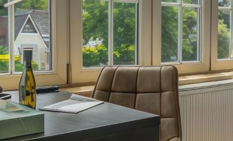 a well - lit room with large windows , white walls , and wooden furniture , including a desk with a chair and a bottle of wine at Hotel Huron