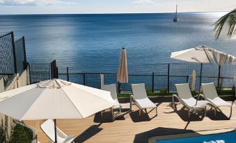 a deck overlooking the ocean , with several lounge chairs and umbrellas set up for guests to enjoy the view at Hotel Pelican