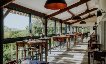 a modern restaurant with wooden tables and chairs , black pendant lights , and large windows offering views of the outdoors at Le Bois d'Imbert