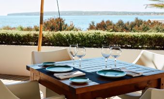 a wooden dining table set with plates , glasses , and napkins on a patio overlooking the ocean at Insotel Hotel Formentera Playa