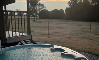 a hot tub is situated on a patio with a fence and trees in the background at Hillcroft Accommodation