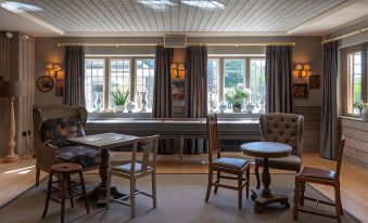 a room with wooden furniture , including chairs and tables , next to large windows that allow natural light to fill the space at The Frogmill Hotel