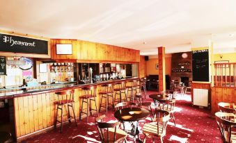 a well - lit bar with wooden walls , a counter filled with drinks , and several stools for patrons to sit on at The Pheasant Inn