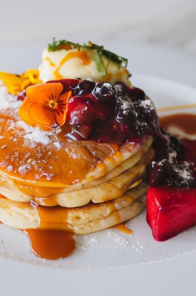 a stack of pancakes with fruit and syrup , accompanied by a cup of coffee on a white plate at Oval Hotel at Adelaide Oval, an EVT hotel