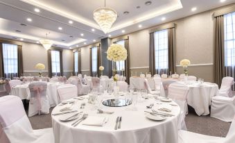 a large , elegant banquet hall with round tables covered in white tablecloths and adorned with white flowers at Villiers Hotel