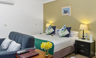 a bed with a green and white headboard is in a room with a blue couch , lamps on either side , and a yellow flower arrangement at Oyster Cove Chalet