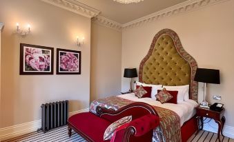 a luxurious bedroom with a large bed , red and gold headboard , white bedding , and two paintings on the wall at Nunsmere Hall Hotel