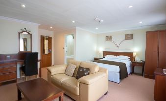 a modern hotel room with a beige couch , wooden table , and bed , along with some office equipment at Beaufort Park Hotel