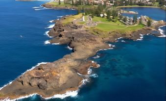 an aerial view of a coastal city with a lighthouse on an island , surrounded by water and buildings at Shellharbour Village Motel