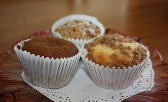 three different types of muffins are displayed on a doily , with one being brown and one having a bite taken out at Westbury Gingerbread Cottages