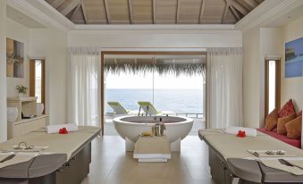 a luxurious spa room with two massage tables , a bathtub , and a view of the ocean at Outrigger Maldives Maafushivaru Resort