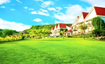 a large , well - maintained green lawn with a few trees and buildings in the background , under a blue sky with clouds at Thunderbird Resorts - Rizal