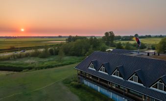 aerial view of a building with a flag on top , surrounded by a grassy field and trees during sunset at Van der Valk Hotel Volendam