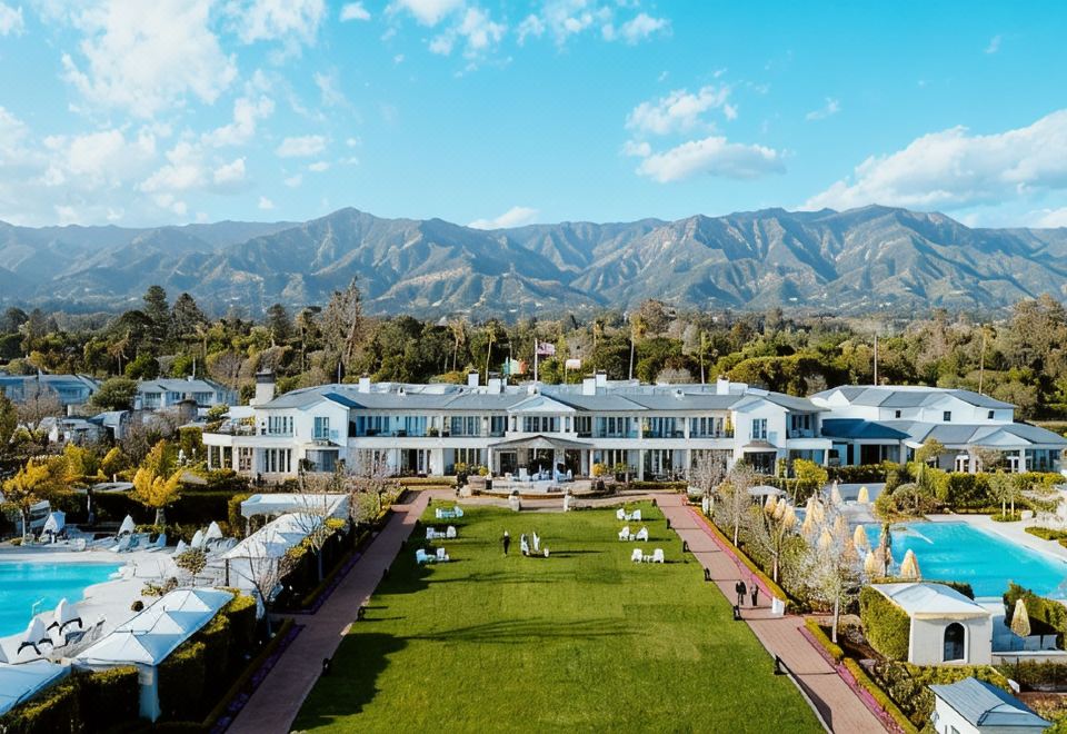 a large white building with a long lawn in front of it and mountains in the background at Rosewood Miramar Beach
