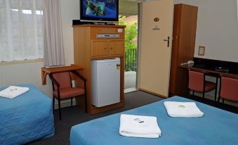 a hotel room with two beds , a small television on the wall , and a door leading to the balcony at Bucketts Way Motel