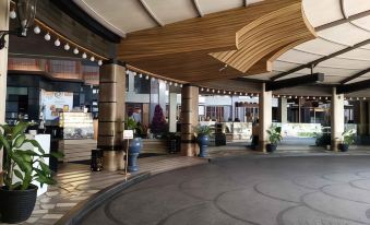 a large , well - lit lobby with a wooden ceiling and stone columns , decorated with potted plants and string lights at Crown Victoria Hotel Tulungagung