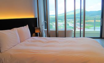 a large bed with a white comforter and pillows is in a room with a window overlooking a cityscape at Am Hotel