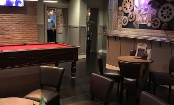 a cozy bar with a pool table , stools , and plants , as well as a tv screen displaying various items on the wall at Caledonian Hotel